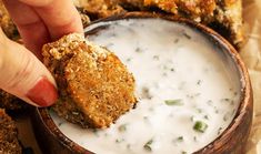 a person dipping something into a bowl of ranch dip with chicken wings in the background