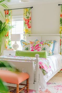 a white bed sitting in a bedroom next to a window with colorful curtains on it