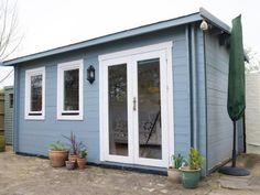 a small blue shed with two doors and some potted plants on the outside patio