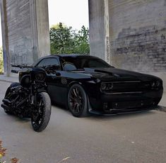 a black car parked next to a motorcycle on the street in front of an overpass