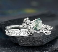 two wedding rings sitting on top of each other with green stone in the middle and leaves around them