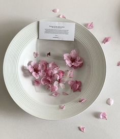 a white plate topped with pink flowers and a piece of paper on top of it