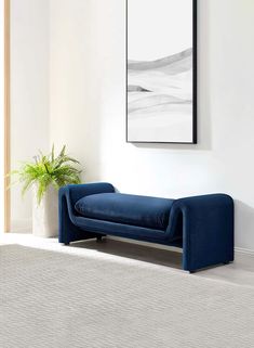 a blue couch sitting next to a plant in a living room under a framed painting