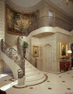 an ornate staircase in the middle of a living room with paintings on the wall and chandelier