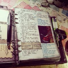 an open notebook with writing on it and some pens sitting next to each other in front of a pile of papers