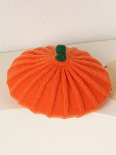 an orange knitted pumpkin sitting on top of a white shelf next to a clock