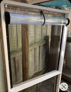 a white window frame with an animal cage in front of it and a black cat sitting on the ledge