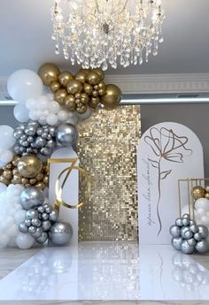 a table topped with balloons and a chandelier filled with gold, silver and white decorations