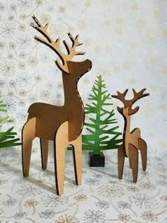 two wooden deer standing next to each other in front of christmas trees and snowflakes