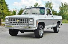 a silver truck parked on the side of a road next to some trees and bushes