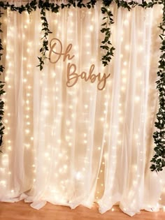 a baby shower curtain with lights and greenery on it that says oh, baby