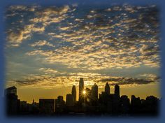 the sun is setting over a city with skyscrapers in the distance and clouds in the sky