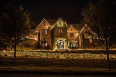 a large house with christmas lights on it's windows and trees in the front yard