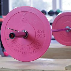 a pink barbell weight plate sitting on top of a wooden table in a gym