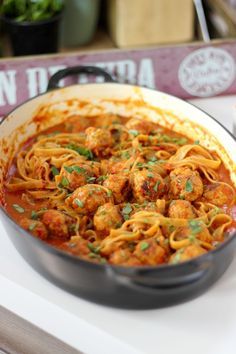 a pan filled with pasta and meat sitting on top of a table next to a sign