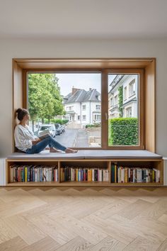 a woman sitting on top of a window sill next to a bookshelf