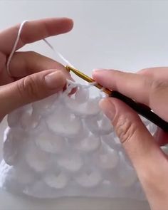 two hands are holding scissors and threading the string to a plastic bag filled with white balls