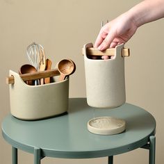 a person is holding a wooden spoon and measuring cup on a table with utensils in it