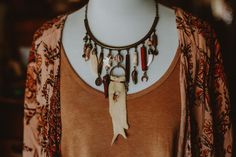 This one of a kind necklace is made from a brushed bronze half circle adorned with all kinds of earthy trinkets, from a carved bone feather, coyote tooth, vertibrae bone, tibetan clay beads, copper charms, peachy crystal and deerskin leather. Length is slightly adjustable. Rustic Brown Healing Necklace, Earthy Electroformed Bronze Necklace, Bohemian Brown Electroformed Necklaces, Southwestern Style Brown Hand-strung Necklace, Brown Agate Hand-strung Necklaces, Half Circle, Deer Skin, Brushed Bronze, Bone Carving