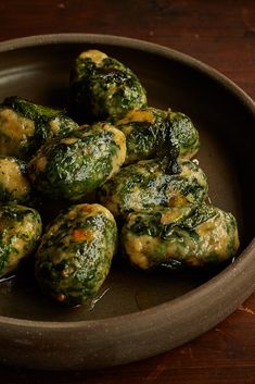 a brown bowl filled with spinach covered in sauce on top of a wooden table