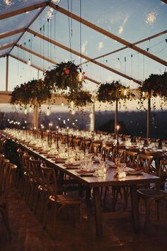 a long table set up with candles and greenery hanging from the ceiling for an outdoor wedding reception