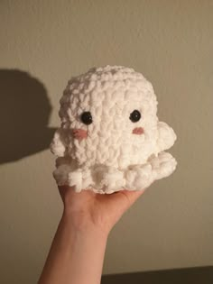 a hand holding a small white crocheted object with eyes on it's face