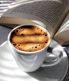 a cup of coffee sitting on top of a saucer next to an open book