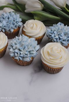 several cupcakes with frosting and blue flowers on them sitting on a table