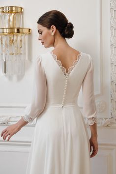 a woman in a white dress standing next to a wall with a light fixture on it