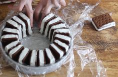 someone decorating a cake with chocolate and marshmallows on the table next to it