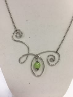 a silver necklace with a green bead hanging from it's center, on a white mannequin