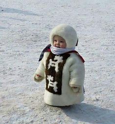 a small child in a snow suit with chinese characters on it's back, standing in the snow