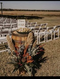 an outdoor ceremony setup with white chairs and wooden barrels filled with flowers on the grass