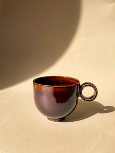 a brown coffee cup sitting on top of a white table next to a shadow from the wall