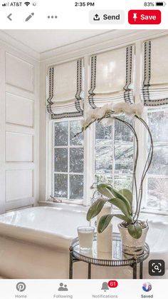 a bath tub sitting next to a window filled with white flowers and greenery on top of a glass table