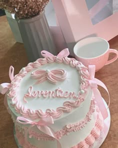 a white cake with pink icing and bows on it sitting next to a cup