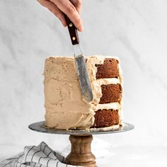 a person is cutting into a cake with a knife on a metal platter and white marble background