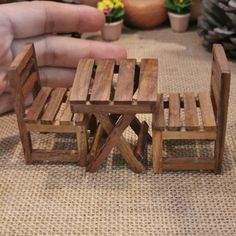 a miniature wooden chair and table made out of pallet wood, with one hand reaching for it