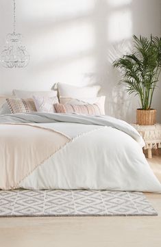 a bed with white sheets and pillows in a room next to a potted plant