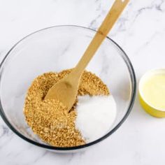 a glass bowl filled with spices next to a wooden spoon on top of a marble counter