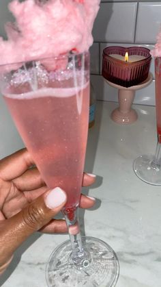 a person holding a wine glass with pink liquid in it and two candles on the table