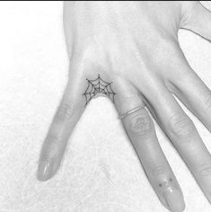 a person's hand with a spider web tattoo on the middle of their finger