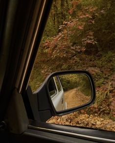 a car is seen in the rear view mirror as it drives down a dirt road