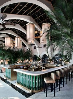 an indoor bar with palm trees in the background and hanging lights on the ceiling above it