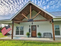 a small white house with an american flag on the front porch and covered porch area