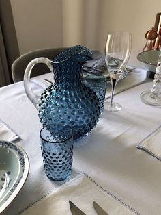 a blue vase sitting on top of a table next to wine glasses and silverware