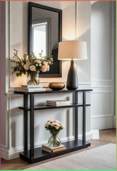 a table with flowers and a lamp on it in front of a mirror that is above the shelf