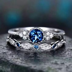 two wedding rings with blue and white diamonds on top of each other, sitting on a rock