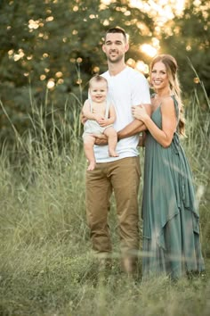 a man and woman holding a baby standing in tall grass