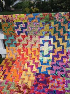 a colorful quilt hanging from the side of a white fence